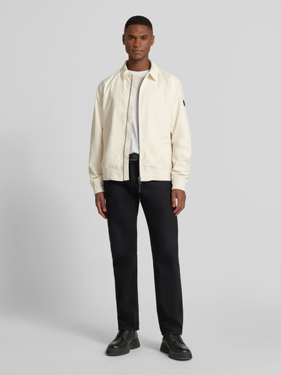 Männermodel trägt Jacke mit Reißverschluss Modell 'Salvador' von JOOP! Collection in Regular-Fit, Kentkragen, Eingrifftaschen, Label-Detail, gerippte Abschlüsse, in Creme und Schwarz, Ganzkörperansicht von vorne.