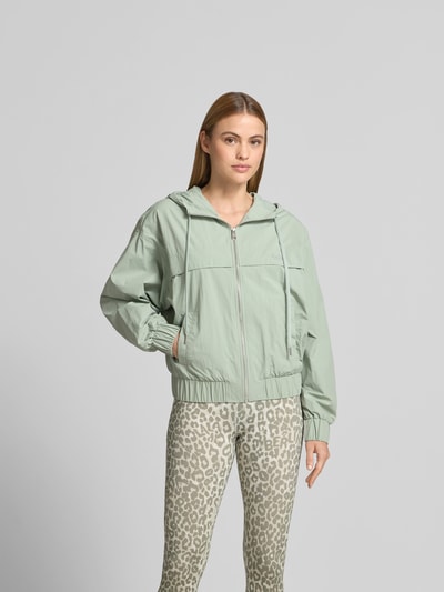 Frauenmodel trägt Regular Fit Jacke mit Logo-Stitching von Lala Berlin in hellem Grün mit Kapuze, Tunnelzug, Reißverschluss, Eingrifftaschen, Rückenlänge 53 cm, Brustweite 60 cm, Ärmellänge 59 cm, Ganzkörperansicht von vorne.