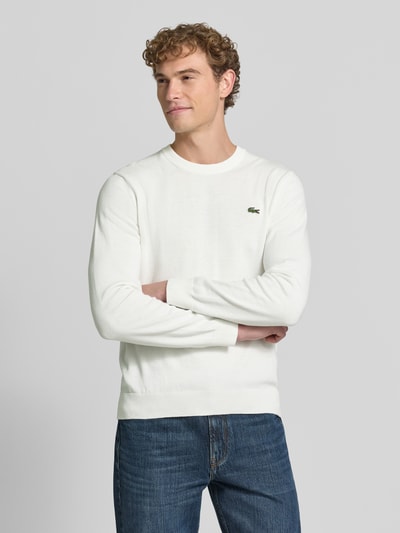 Männermodel trägt weißen Regular Fit Pullover aus Baumwoll-Mix von Lacoste, kombiniert mit blauer Jeans, Ganzkörperansicht von vorne. Herren Pullover von Lacoste