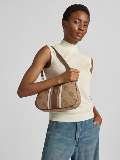 Frauenmodel trägt Shoulder Bag in Leder-Optik Modell 'Noelle' von GUESS mit Logo-Detail, Hauptfach mit Reißverschluss, beige-braune Farbtöne, strukturiertes Material, abnehmbarer Schulterriemen, Ganzkörperansicht von vorne.