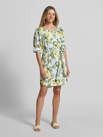 Frauenmodel trägt Minikleid mit Bindegürtel von Marc Cain aus Baumwolle mit Allover-Zitronenmuster, geradem Schnitt und Rundhalsausschnitt, Ganzkörperansicht von vorne.