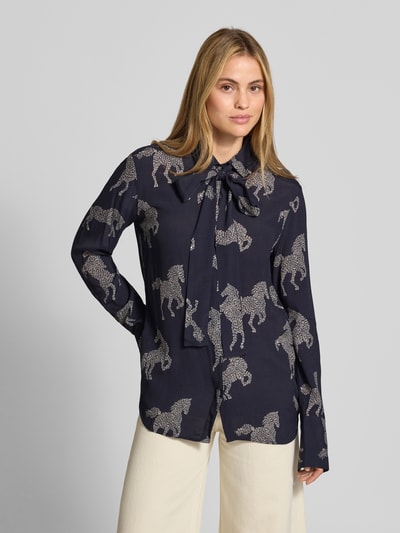 Frauenmodel trägt Relaxed Fit Bluse aus reiner Viskose Modell 'ODETTA' von ODETTA mit Allover-Motiv-Print, dunkelblau-creme, Zierschleife, Langarm, Ganzkörperansicht von vorne.