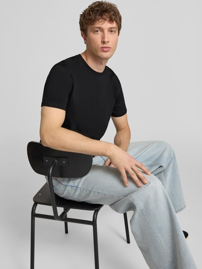 Männermodel trägt T-Shirt mit Label-Patch von Alpha Industries, czarna bawełna, prosty krój, okrągły dekolt, Ganzkörperansicht von vorne