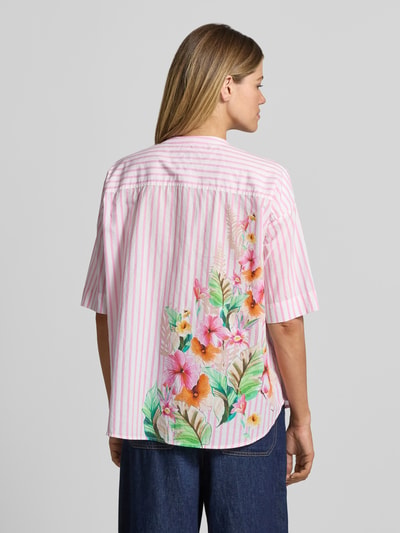 Frauenmodel trägt Relaxed Fit Bluse mit Motiv-Print und Tunikakragen von Emily Van den Bergh aus reiner Baumwolle, rosa-weiß gestreift mit farbigem Blumenmuster, Ganzkörperansicht Rückansicht.