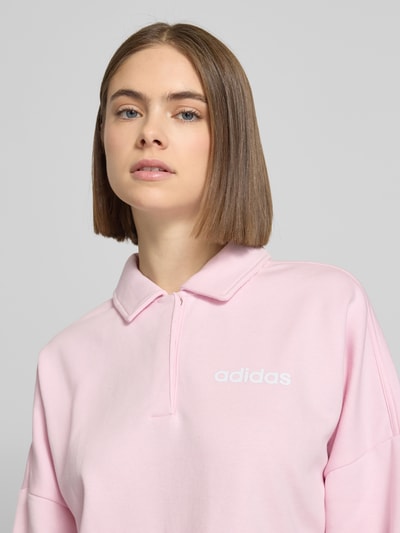 Frauenmodel trägt Sweatshirt mit Label-Print von adidas Sportswear in Rosa, locker geschnitten aus reinem Rayon, Nahaufnahme Oberkörper.