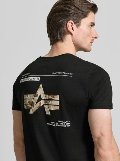 Männermodel trägt T-Shirt mit Label-Patch Modell 'Camo' von Alpha Industries, schwarze Baumwolle, Print hinten, Ganzkörperansicht Rückansicht.