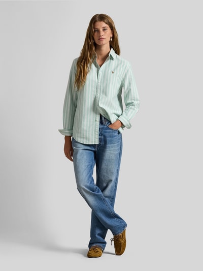 Kobiece model prezentuje Regular Fit Hemdbluse aus reiner Baumwolle von Polo Ralph Lauren, wzór w paski, wyhaftowane logo, krój regular fit, kołnierzyk koszulowy, listwa guzikowa, długi rękaw z mankietem, wykończenie Oxford, efekt: wzór na całej powierzchni, czysta bawełna, jasne pasy, gładka faktura, widok całej sylwetki z przodu.