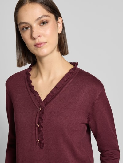 Frauenmodel trägt Regular Fit Pullover mit Woll-Alpaka-Anteil Modell 'Katie' von FREE/QUENT, bordeaux, Strick-Optik, V-Ausschnitt, Rüschenbesatz, Knopfleiste, Material-Mix, Nahaufnahme Oberkörper.