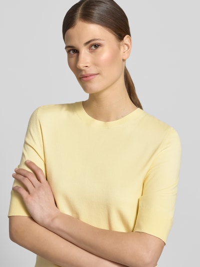 Vrouwenmodel draagt Slim Fit Strickpullover aus Viskose-Mix van s.Oliver RED LABEL, effen lichtgeel, fijne breistructuur, ronde hals, korte mouw, geribde boorden, nahaufnahme bovenlichaam.