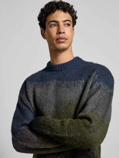 Männermodel trägt Strickpullover mit Rundhalsausschnitt Modell 'TINLEY' von Carhartt Work In Progress, melierte Farben, Nahaufnahme Oberkörper. Herren Strickpullover mit geradem Schnitt, Materialmix mit Alpaka-Anteil.
