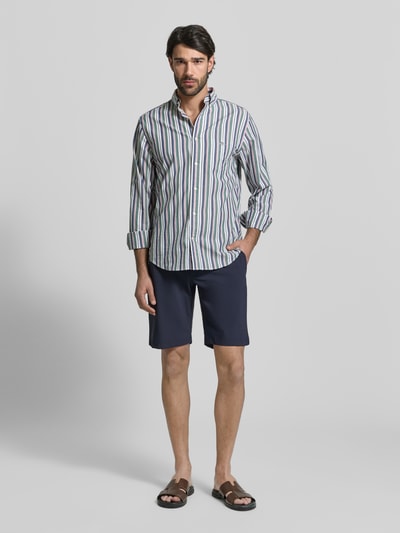 Męski model nosi Straight Fit Shorts mit elastischem Bund von CRUNA, granatowy kolor, kieszenie z tyłu, szerokość w rozmiarze 50: 42 cm, długość wewnętrzna nogawki w rozmiarze 50: 26 cm, krój straight fit, całkowity widok z przodu