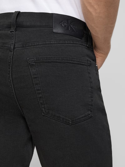 Männermodel trägt Slim Fit Jeansshorts aus Baumwoll-Mix Modell 'CK ESSENTIAL BLACK' von Calvin Klein Jeans in schwarzer Denim-Optik mit Label-Patch, sichtbare Nahtdetails und 5-Pocket-Design, Detailaufnahme Rückansicht.