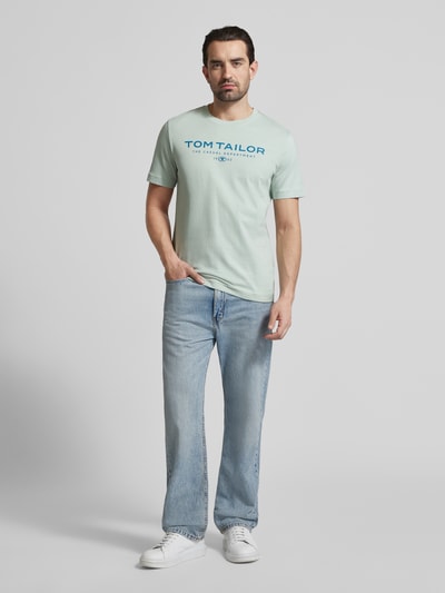 Männermodel trägt Regular Fit T-Shirt aus reiner Baumwolle von Tom Tailor in Optik: Unifarben mit Label-Print, Rundhals, Ganzkörperansicht von vorne.