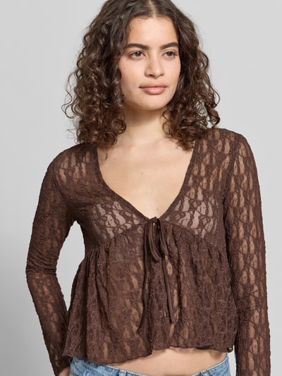 Frauenmodel trägt Shaped Fit Blusentop mit Bindeverschluss Modell 'LAYA' von Only, braun, abstraktes Muster, Semitransparent, Mesh-Optik, Langarm, Ohne Kragen, tiefer V-Ausschnitt, Nahaufnahme Oberkörper.