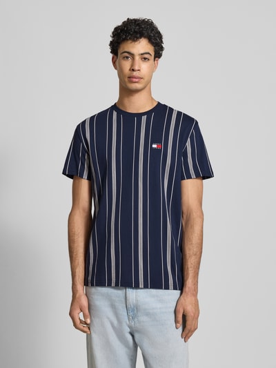 Männermodel trägt Regular Fit T-Shirt aus reiner Baumwolle von Tommy Jeans, Optik: Allover-Muster, Label-Stitching-Applikation, Rundhals, Kurzarm, Ganzkörperansicht von vorne.