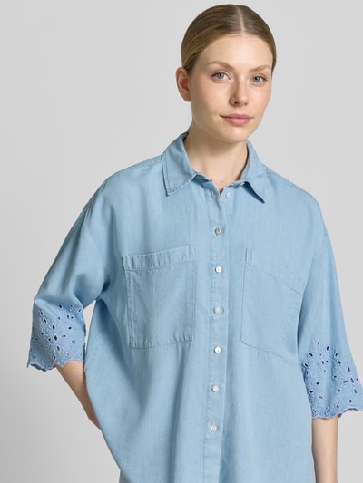 Kobiece modelka nosi bluzka jeansowa 'Jeansbluse mit Lochstickerei und Hemdblusenkragen' od Smith and Soul, reines lyocell, krój loose fit, kołnierzyk koszulowy, listwa guzikowa, kieszenie na piersi, haft angielski na rękawach, długość tyłu w rozmiarze S 61 cm, długość rękawów w rozmiarze S 34 cm, jasnoniebieski kolor, gładka struktura, widoczne detale, zbliżenie na górę ciała.