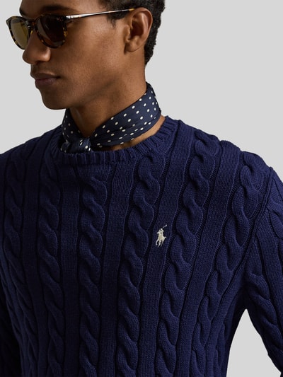Mężczyznamodel nosi Regular Fit Strickpullover aus reiner Baumwolle von Polo Ralph Lauren w kolorze granatowym, wzór warkoczowy, logo, okrągły dekolt, dzianina, czysta bawełna, krój regular fit, widok z przodu, zbliżenie na górną część ciała.