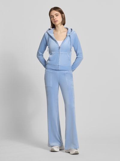Frauenmodel trägt Low Rise Sweatpants mit Eingrifftaschen Modell 'LAYLA' von Juicy Couture, Damen Sweatpants aus Material-Mix mit Stretch-Anteil, Elastikbund, hellblau, glatt mit leichten Nähten, Ganzkörperansicht von vorne. Innenbeinlänge bei Größe S: 82 cm.