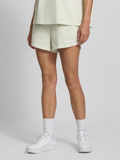 Frauenmodel trägt High Waist Sweatshorts mit Logo-Stitching Modell 'WILUNA' von Pegador aus Baumwoll-Mix, elastischer Bund, Bundweite bei Größe S: 38 cm, Nahaufnahme Oberschenkel.