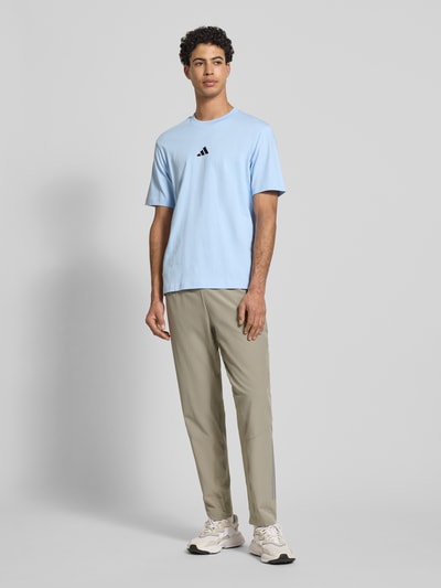 Männermodel trägt T-Shirt mit Label-Detail von adidas Sportswear in Hellblau, reine Baumwolle, Regular Fit, Ganzkörperansicht von vorne.