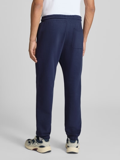 Männermodel trägt Straight Fit Sweatpants aus Baumwoll-Mix Modell 'Kane' von JACK & JONES in Dunkelblau, Gesäßtasche, elastischer Bund und Beinabschlüsse, Ganzkörperansicht Rückansicht.