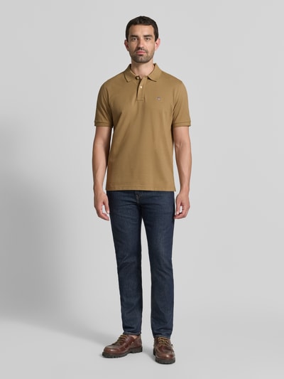 Mannelijk model draagt Regular fit poloshirt uit puur katoen van GANT in bruin met korte mouwen, donkere jeans, Ganzkörperansicht von vorne.