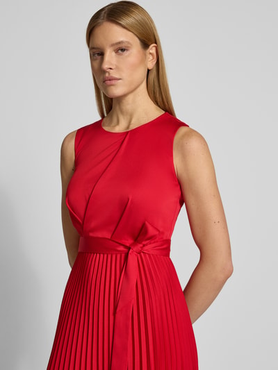 Modelka nosi 'Cocktailkleid mit Plisseefalten' od Vera Mont, czerwień, marszczenia, pasek w talii, krój slim fit, plisy, zbliżenie na górę ciała.
