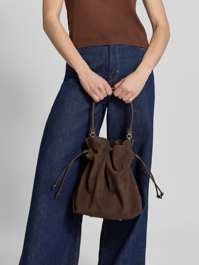 Frauenmodel trägt Handtasche in Suede-Optik Modell 'Cool Companion' von Hey Marly in Dunkelbraun, einfache Form, samtige Textur, Hauptfach mit Magnetverschluss, abnehmbarer Schulterriemen, Innenfach mit Reißverschluss, Maße 40x34x15 cm, Ganzkörperansicht von vorne.