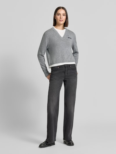 Frauenmodel trägt Relaxed Fit Strickpullover mit Woll-Anteil von Oui in Grau mit V-Ausschnitt, Label-Stickerei, gerippten Abschlüssen, langärmeligem Design, kombiniert mit dunkler Jeans, Ganzkörperansicht von vorne.