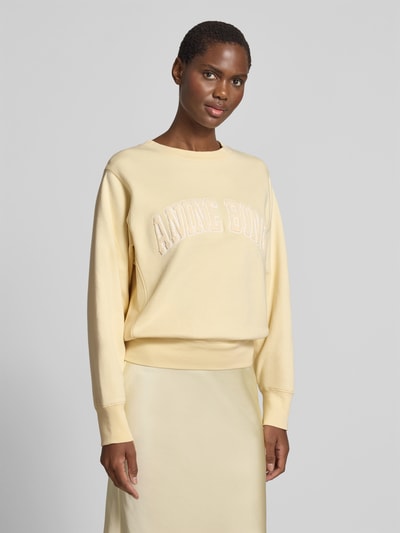 Frauenmodel trägt Regular Fit Sweatshirt mit Logo-Detail von Anine Bing in hellem Gelb, reine Baumwolle, Rundhalsausschnitt, elastische Abschlüsse, Ganzkörperansicht von vorne.