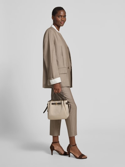 Frauenmodel trägt Bucket Bag mit Logo-Detail Modell 'Romy' von Tory Burch in Beige mit Strukturmuster, abnehmbarem Schulterriemen, Ganzkörperansicht von vorne.