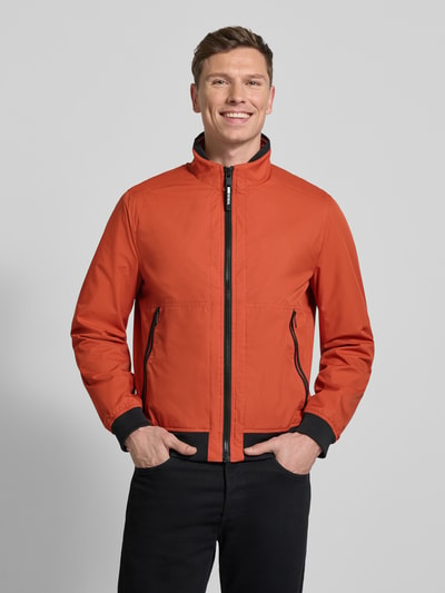 Männermodel trägt Regular Fit Jacke mit Stehkragen von MCNEAL in Orange, sichtbare Reißverschlusstaschen, elastische Abschlüsse, Ganzkörperansicht von vorne.