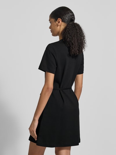 Vrouwenmodel draagt Tailliertes Sweatkleid aus reiner Baumwolle van Tommy Hilfiger in effen zwart, taillering, mini-lengte, korte mouw, ronde hals, logo-stiksel, zonder sluiting, bindceintuur, rechte zoom, interlock van zuiver katoen, totaalbeeld achteraan.