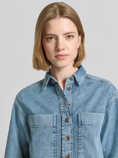 Frauenmodel trägt Relaxed Fit Hemdbluse in Denim-Optik von Emily Van den Bergh, Reine Baumwolle, Hemdblusenkragen, Halbarm, Brusttaschen, durchgängige Knopfleiste, Nahaufnahme Oberkörper.