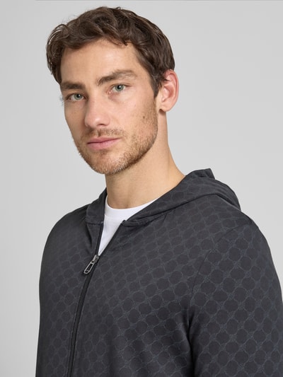 Männermodel trägt Sweatjacke mit Logo-Muster und Kapuze von JOOP! Collection aus Reiner Baumwolle, Regular-Fit, Nahaufnahme Oberkörper.