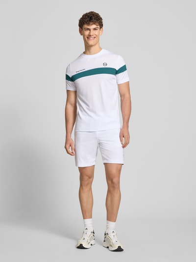 Männermodel trägt Regular Fit T-Shirt mit Logo-Print Modell 'Leone' von SERGIO TACCHINI in Weiß mit grünen Streifen, Rundhals, Ganzkörperansicht von vorne.