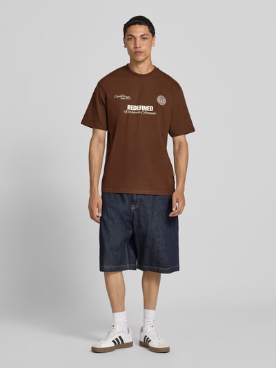 Männermodel trägt T-Shirt mit Statement-Print und Rundhalsausschnitt von Redefined Rebel, Baumwoll-Mix, Relaxed-Fit, Modell 'Bruno', braun, Herren T-Shirt, Rückenlänge 70 cm bei Größe M, Ganzkörperansicht von vorne.