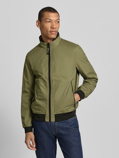 Männermodel trägt Regular Fit Jacke mit Stehkragen von MCNEAL in Olivgrün mit Reißverschluss und elastischen Abschlüssen, Ganzkörperansicht von vorne, Rückenlänge bei Größe M 64 cm, Schulterbreite 43 cm, Brustweite 55 cm, Ärmellänge 67 cm.