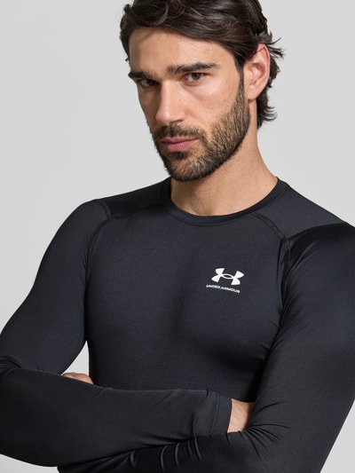 Männermodel trägt Slim Fit Longsleeve mit Logo-Print von Under Armour, elastischer Material-Mix, Rundhalsausschnitt, Nahaufnahme Oberkörper.