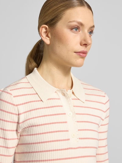 Frauenmodel trägt Regular Fit Poloshirt mit Streifenmuster Modell 'Caliz Stripe' von MOS MOSH, creme-rosa, feine Rippenstruktur, Nahaufnahme Oberkörper. Viskose-Mix mit Seiden-Anteil, Knopfleiste, Rückenlänge 58 cm, Ärmellänge 29 cm.