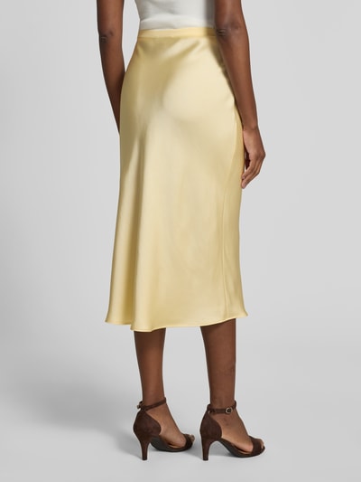 Frauenmodel trägt Midirock aus Satin von Anine Bing in Gelb mit glänzender Optik, figurbetonter Passform, elastischem Bund, Midilänge, Rückansicht Ganzkörperansicht.