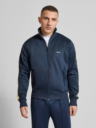 Męski model nosi Track Jacket mit Stretch-Anteil Modell 'Everyday' von ANOTHER COTTON LAB, granatowy, elastyczna mieszanka materiałów, prosty krój, zamek błyskawiczny, kieszenie zapinane na zamek błyskawiczny, lampasy, aplikacja z metką, długość tyłu w rozmiarze M: 63 cm, długość rękawów w rozmiarze M: 68 cm, zdjęcie: całkowity przód