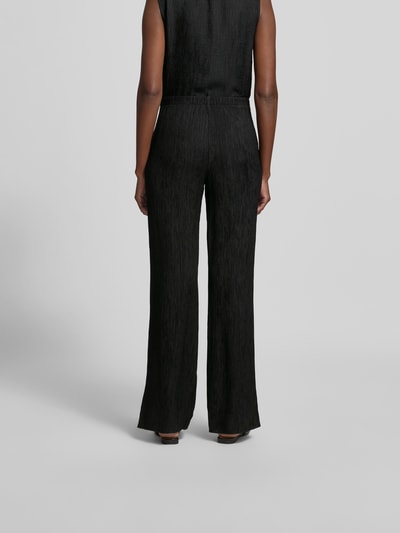 Frauenmodel trägt Straight Fit Stoffhose aus Viskose-Mix von Anine Bing mit Strukturmuster, elastischem Bund und Eingrifftaschen, Ganzkörperansicht Rückansicht.