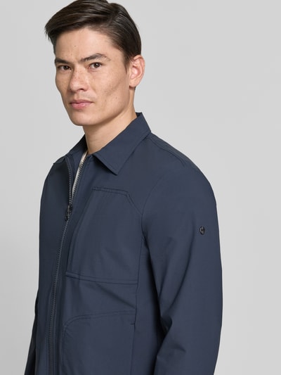 Männermodel trägt Regular Fit Jacke mit Umlegekragen Modell 'Motion' von SCANDINAVIAN EDITION in Dunkelblau, Nahaufnahme Oberkörper. Elastischer Material-Mix, Napoleontasche, Zweiwege-Reißverschluss und Eingrifftaschen sind sichtbar.