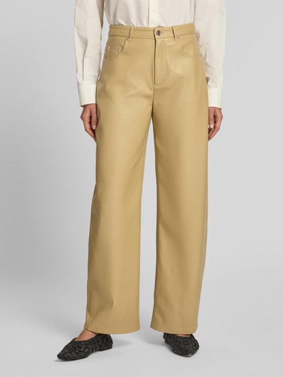 Frauenmodel trägt Straight Fit Hose in Leder-Optik von Nanushka in Beige mit 5-Pocket-Design, Gürtelschlaufen, Knopf- und Reißverschluss, Ganzkörperansicht von vorne.