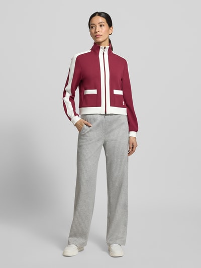 Frauenmodel trägt Regular Fit Sweatjacke mit Stehkragen von Marc Cain in Rot und Weiß, elastischer Material-Mix, Ganzkörperansicht von vorne.