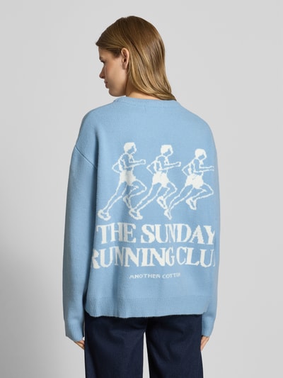 Frauenmodel trägt Oversized Strickpullover mit Rückenmotiv von ANOTHER COTTON LAB in Hellblau mit Rundhalsausschnitt und Label-Stitching, Rückenlänge 62 cm, Ärmellänge 57 cm, Ganzkörperansicht Rückansicht.