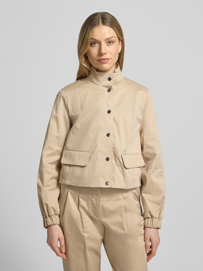Frauenmodel trägt Regular Fit Jacke mit Stehkragen von Marc Cain aus elastischem Baumwoll-Mix in Beige, mit Pattentaschen, Knopfleiste, Logo-Applikation und elastischen Ärmelabschlüssen, Ganzkörperansicht von vorne.