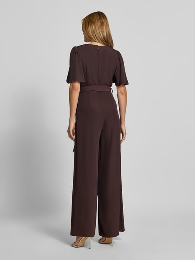 Frauenmodel trägt Jumpsuit mit Stoffgürtel von Rinascimento, braune Farbe, lockerer Material-Mix mit Stretch, tailliert, Kurzarm, Ganzkörperansicht Rückansicht. Damen Jumpsuit, V-Ausschnitt, Raffungen, Rückenlänge S 148 cm, Brustweite S 37 cm, Ärmellänge S 30 cm, Gesamtlänge S 147 cm, Innenbeinlänge S 79 cm.