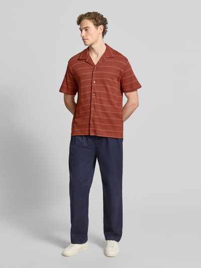 Männermodel trägt Relaxed Fit Freizeithemd aus Baumwoll-Mix mit Viskose-Anteil Modell 'MARC' von Selected Homme in Rot mit feinen Linien, kombiniert mit dunkelblauer Hose und weißen Schuhen, Herren Freizeithemd von Selected Homme, Ganzkörperansicht von vorne.